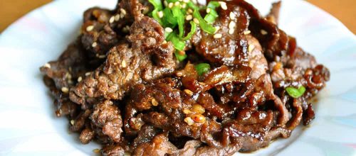 Cooked bulgogi on white blueish plate topped with chopped green onions