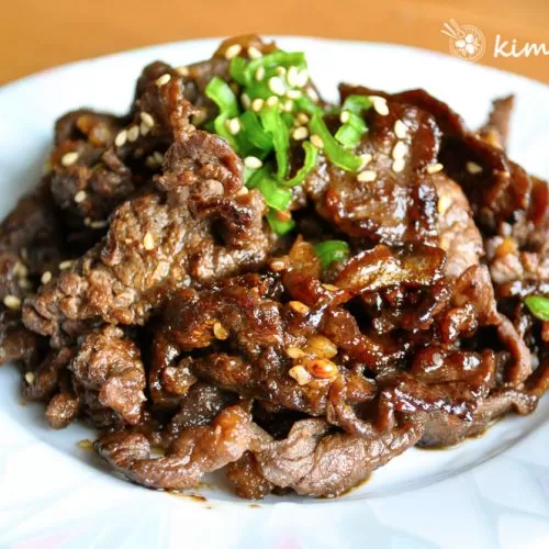 Cooked bulgogi on white blueish plate topped with chopped green onions