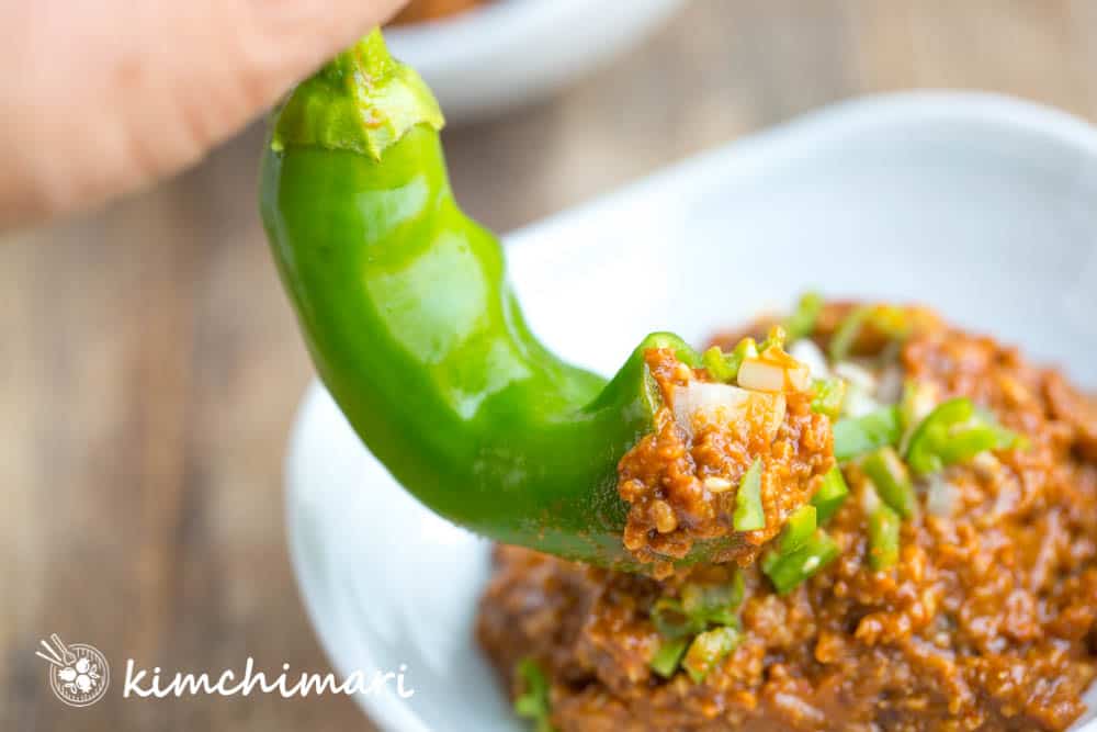 green chili pepper being dipped into ssamjang in white bowl