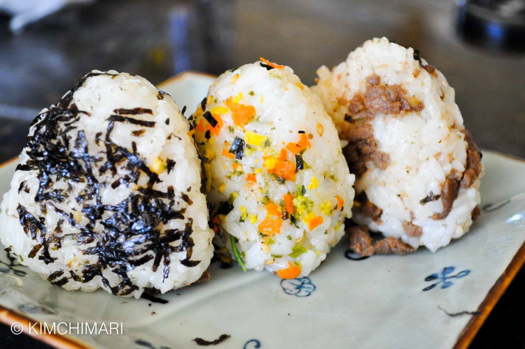 A photo of three triangle shaped rice balls--each ball has a different flavoring. Once has seaweed, one has carrots, and one has beef. 