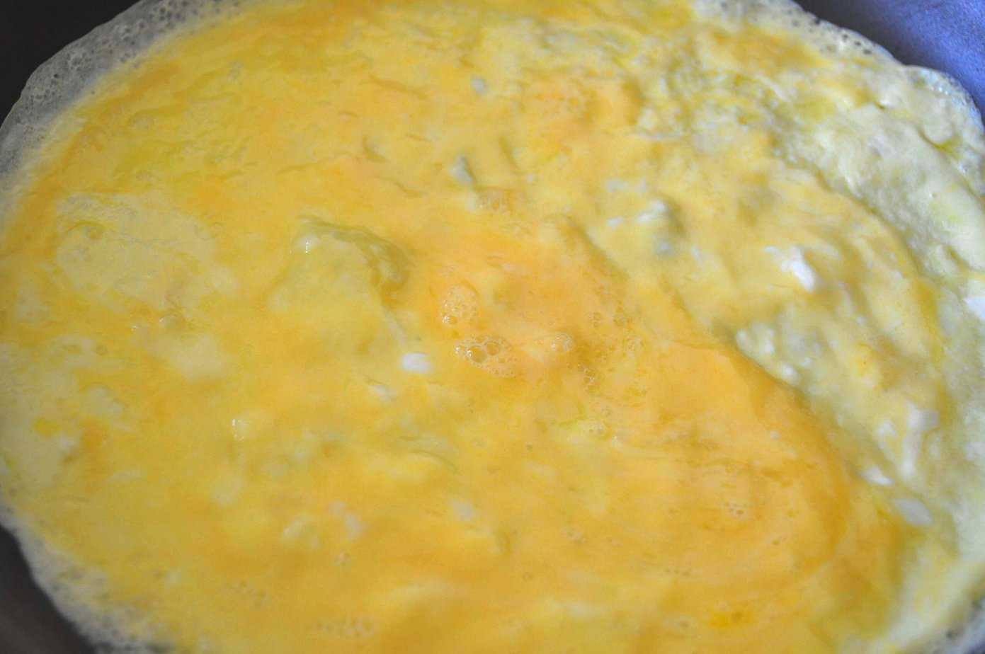 whipped egg spread out on pan cooking