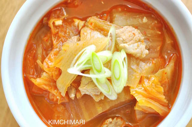 Kimchi Jjigae (Kimchi Stew with Pork Belly) in white bowl topped with green onions