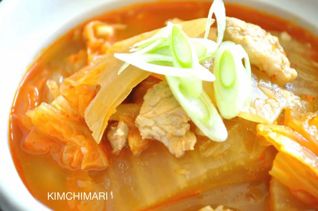 close up of Kimchi Jjigae in white bowl garnished with fresh green onion slices
