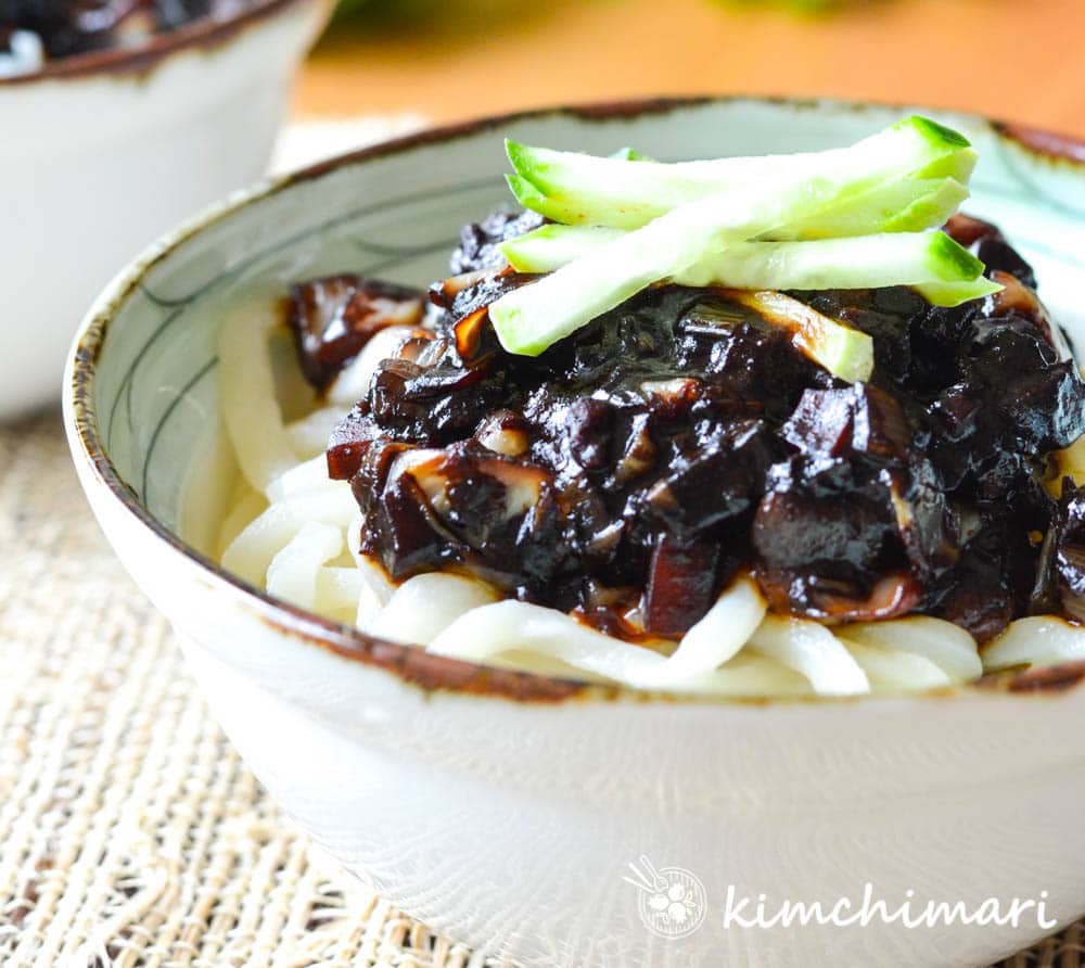 Jjajangmyeon noodles with black bean sauce in white bowl topped with cucumber garnish