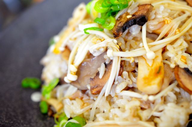 closeup of mushroom rice plated on black plate sprinkled with green onions