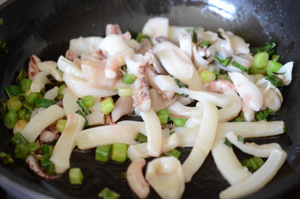 squid stir frying in pan with green onions