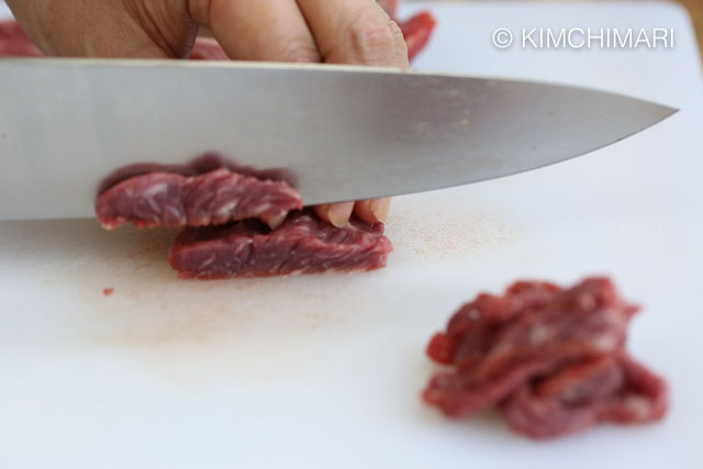 Slicing beef with knife on white cutting board