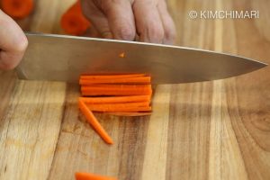 Julienning carrot with knife on cutting board