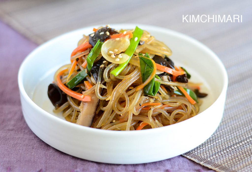 japchae glass noodles in white bowl on light purple linen