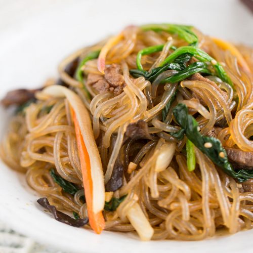 Close up of Japchae with beef and vegetables plated on white plate