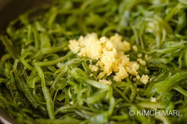 a mound of chopped garlic on top of sauteed seaweed in pan