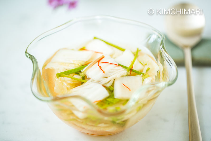 closeup of nabak kimchi in glass bowl with a place setting of spoon