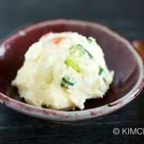 potato salad served as a scoop using ice scream scooper on red ceramic bowl