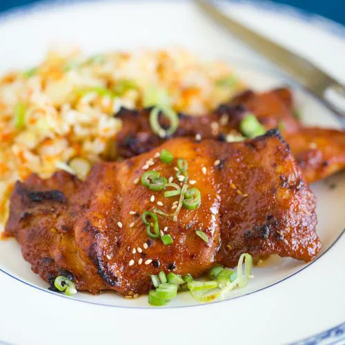 baked spicy chicken thighs plated with simple carrot fried rice