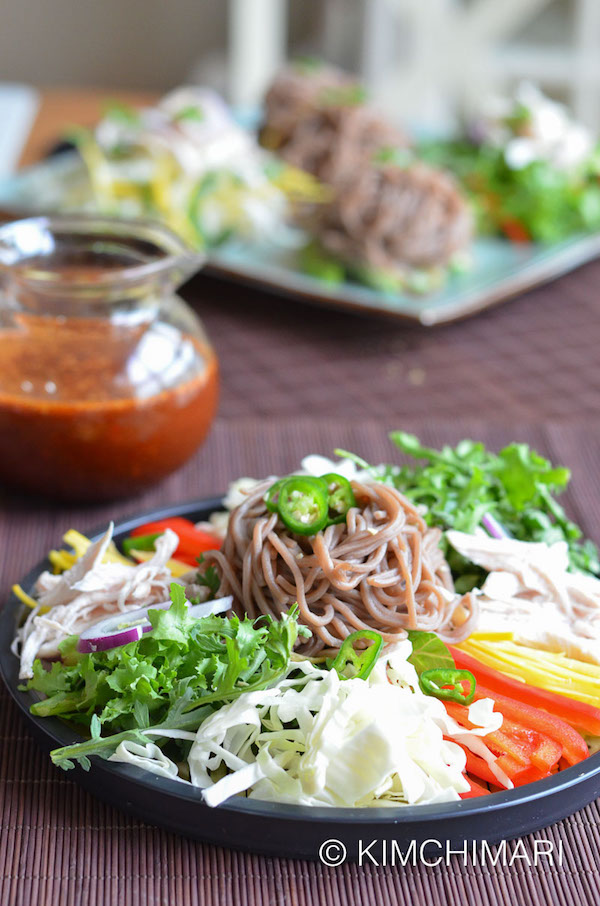 makguksu buckwheat noodles plated with noodles in the center and veggies placed around it