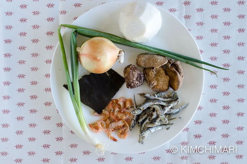 plate of ingredients for broth - dried anchovies radish onion shitake green onion kelp dried shrimps 