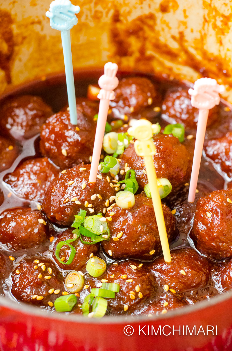 Korean meatballs appetizer finished in pot, garnished with green onions, sesame seeds and with cocktail toothpicks