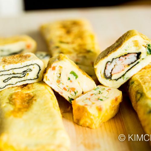 3 different Korean egg roll (gyeran mari) variations of seaweed, carrots and ham and crabmeat cut into slices on cutting board