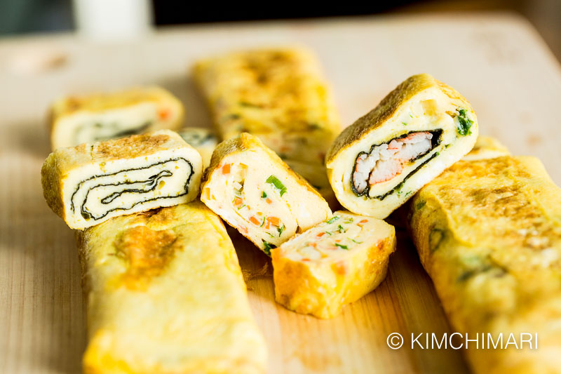 3 different egg roll variations of seaweed, carrots and ham and crabmeat cut into slices on cutting board