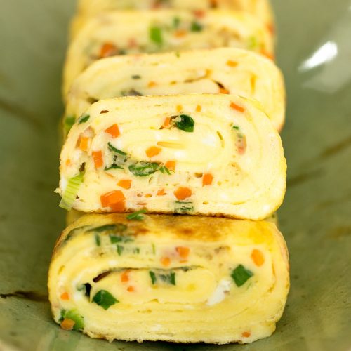 korean egg roll with carrots, ham and green onion cut into slices and plated on green dish