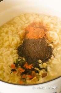 noodles boiling in pot with soup and dry flakes packets all added