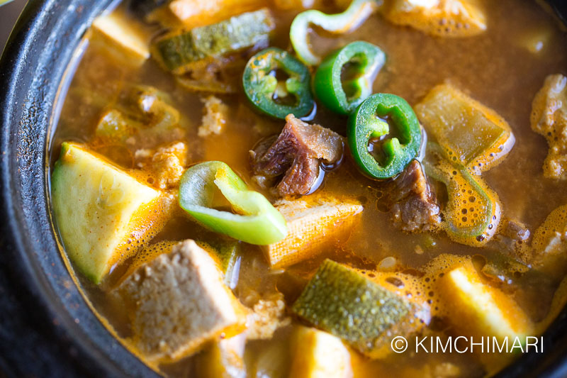 Close up of soybean paste stew topped with fresh green chilis and green onions