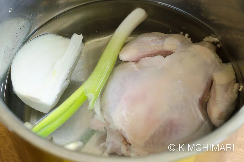 instant pot filled with water, chicken, onion, garlic and green onion