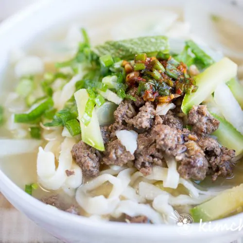 Finished Kalguksu in bowl topped with ground beef, green onions and fresh garlic with chopsticks on top