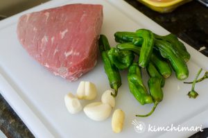eye of round beef, garlic, ginger, shishito peppers on white cutting board