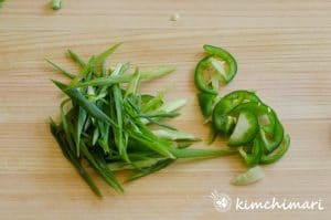 diagonally cut green onions and thinly sliced green chili peppers on wood cutting board