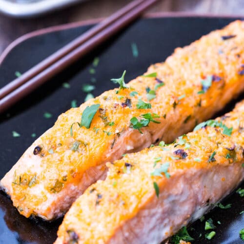 baked salmon fillet on black plate with chopsticks on side