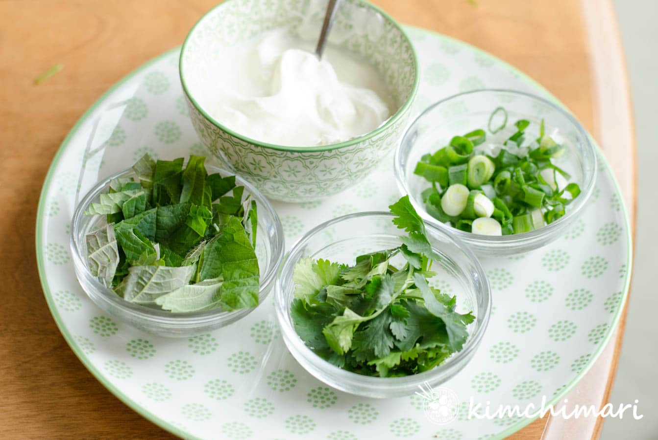 small bowls of chopped herbs and sour cream on green patterened plate