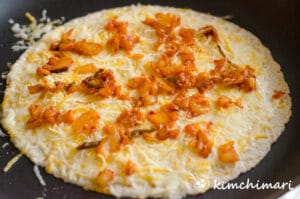kimchi and cheese spread on tortilla in pan
