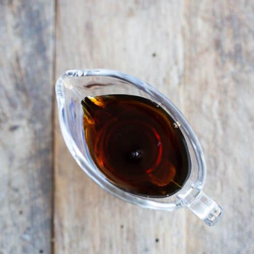 anchovy fish sauce in small glass gravy boat on wooden surface