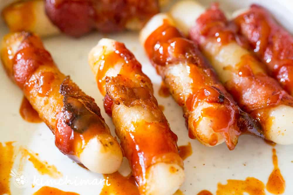 closeup of bacon tteoks served with gochujang sauce drizzled on top