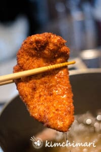 fried chicken katsu held between chopsticks right out of oil