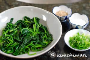 cooked spinach with seasonings in small bowls to make Korean spinach side dish