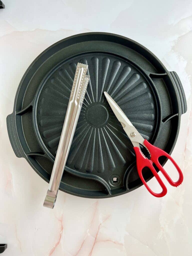 korean grill pan with scissors and tongs laid on top