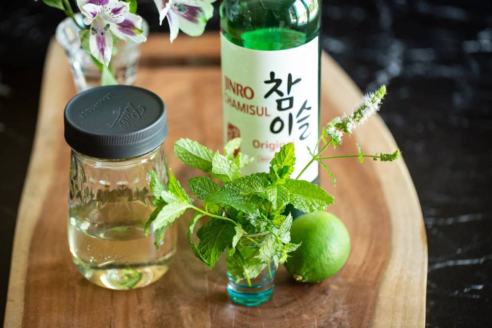 ingredients for soju mojito cocktail on wooden board - lime, mint, soju, simple syrup