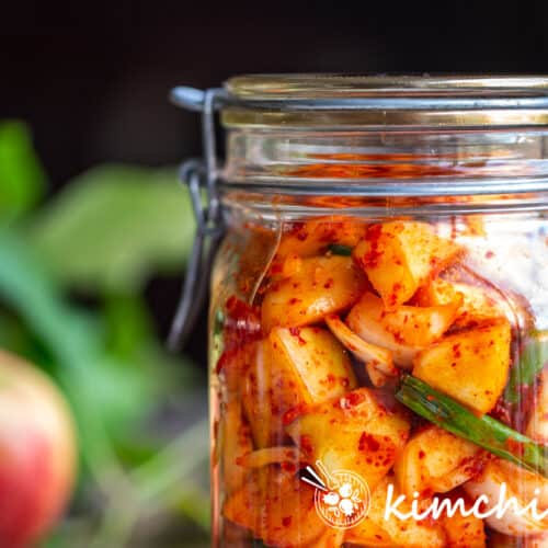 apple kimchi in glass jar with an apple in the background