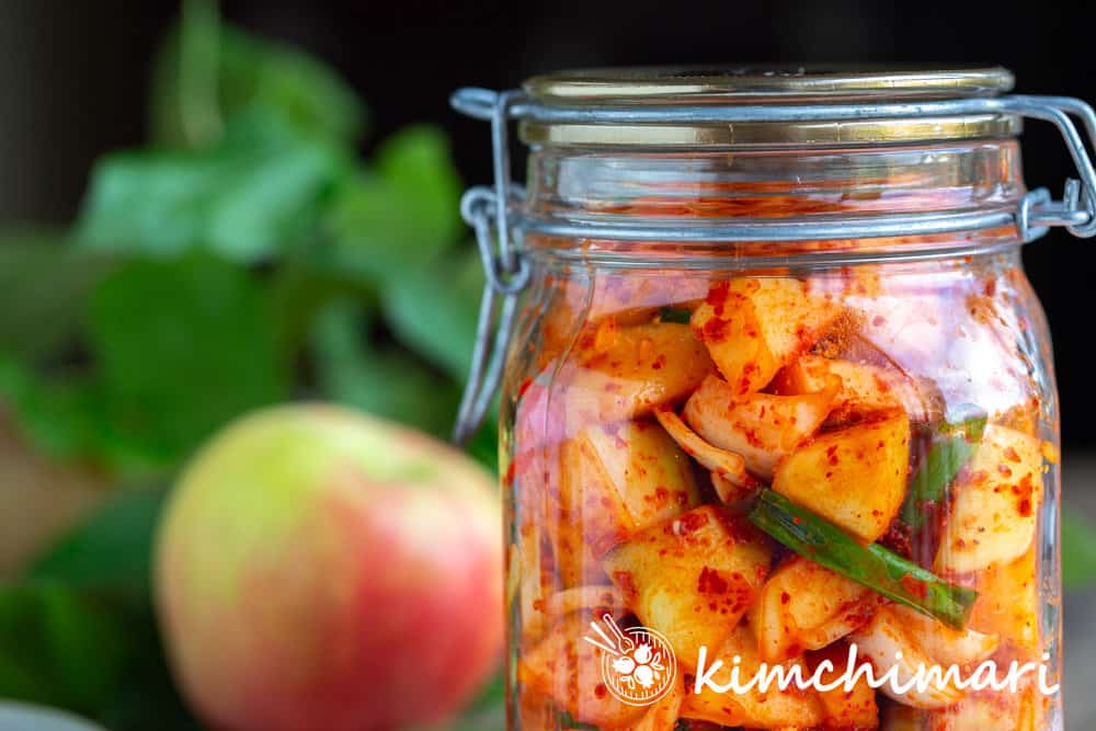 apple kimchi in glass jar with apple tree and leaves in the background