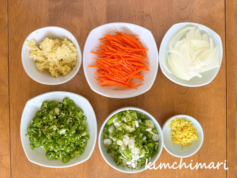 chopped garlic, green chili, green onions, ginger, carrots, onions in small plates on wood table